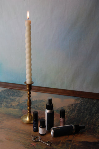 Aromatherapy items like lavender essential oil, pulse point oils and pillow mists next to a candlestick.