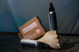 Rose Gold Satin Pillowcase stylized with two bottles of deep sleep pillow spray and a seashell.