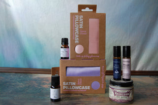 A collection of beauty products, including a rose gold and lavender pillowcase stylized next two magnesium body butter and essential oils.