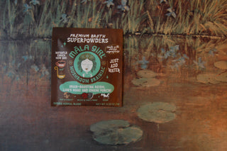 Package of Mala Girl Mushroom Brainiac superpower broth boosted with mushrooms against pond painting.