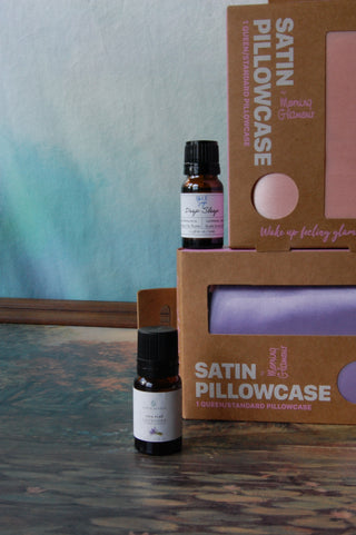 A bottle of Blue Sage's Deep Sleep Essential oil shown next to a bottle of Sixth Scent's Lavender Oil and two boxes of satin pillowcases.