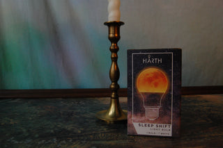 Harth Sleep Shift Amber Light Bulb packaging next to a candlestick.