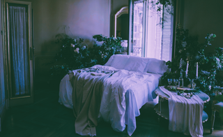 Romantic bedroom with greenery, decorated with a nightstand, candles and dreamy snacks.
